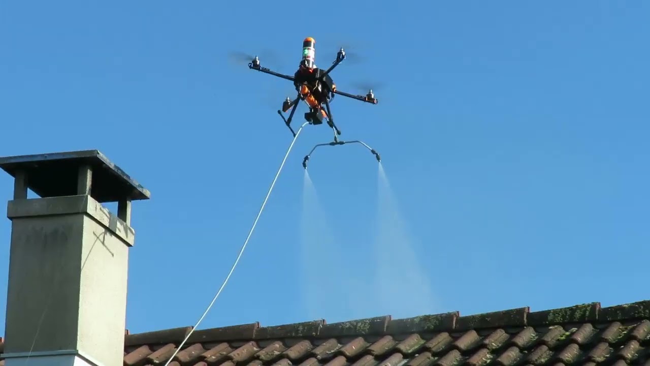 Drone relié au sol par un tuyau, pulvérisant par deux buses le faîtage moussu d'une toiture en tuiles, près d'une cheminée